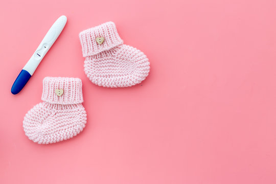 Positive pregnancy test. Baby girl concept with pink booties on pink background top-down copy space