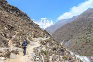 Middle-aged woman walks on footpath from Everest base campin Himalayas. Everest and Lhotse mountain peaks are visible in the background. Imja Khola river flows in valley. Trekking in Nepal theme.