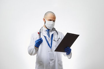 A doctor in a face mask searching for results about a coronavirus blood test in his hand. A portrait of an infectious disease physician holding a positive COVID-19 blood sample and a clipboard.