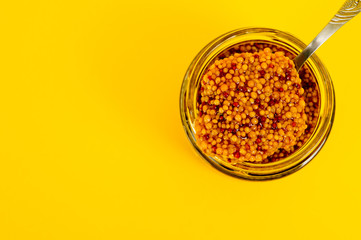 French mustard in a glass jar, shot on a yellow background. Background for seasoning and nutrition.