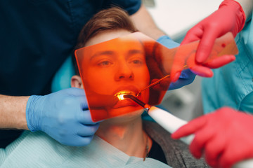 Dentistry. Dentist and patient. Light curing seal. UV dental lamp and orange protect glass. Dental fillings.
