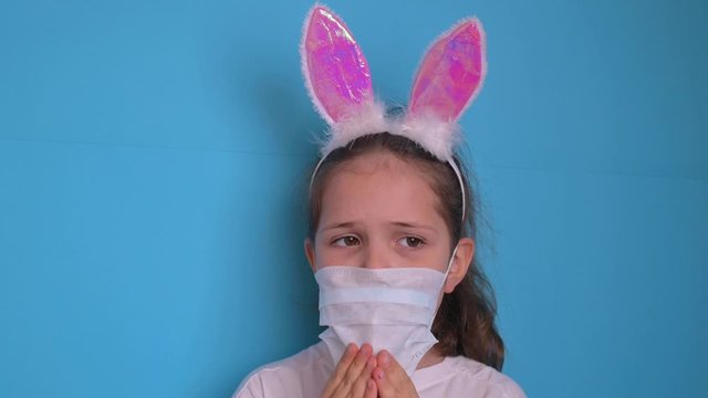 Baby in coronavirus. World pandemic concept COVID 19. Little girl in a protective medical mask closes her eyes with her hands. Emotion baby ea photo. Copy space and blu background . 4k