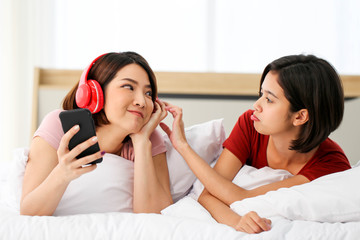 Obraz na płótnie Canvas Happy Couple asia woman wear headphones and enjoy musics playing mobile phone and tablet in bedroom.