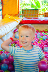 Fototapeta na wymiar A fair haired boy of three years in a game center plays in a pool with colored plastic balls