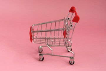 Small trolley with a shopping basket for buy in store on a pink background