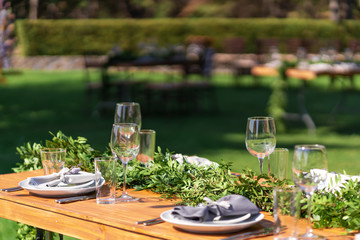 Beautifully decorated wooden table in a summer open-air cafe. Green branch and fresh flowers table decoration