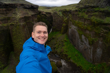 Naklejka premium Young smiling man with river and green canyon on background takes a Selfie. Concept of freedom movement and freedom