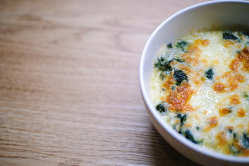 Top view of Baked Spinach with Cheese on wooden texture with copy space for text.