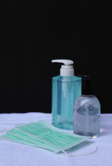 Closeup of surgical face masks  and bottles of alcohol gel on white cloth with black wall background.  Preparation for prevention of COVID-19 outbreak around the World. Vertical view.