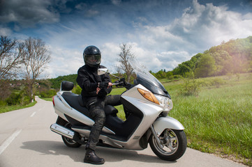 Close Up view of front of motor biker in helmet on motorcycle standing on edge of highway and looking on horizon with mountains