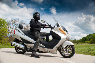 Close Up view of front of motor biker in helmet on motorcycle standing on edge of highway and looking on horizon with mountains