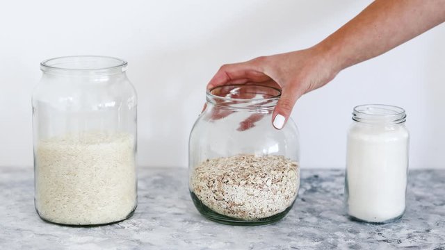 non-perishable pantry ingredients, glass jars with oats flour and rice and hand grabbing the oats