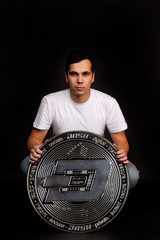 A young guy holds a symbol of the DASH coin, a modern currency for exchange and purchases