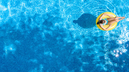 Active young girl in swimming pool aerial top view from above, child relaxes and swims on inflatable ring donut and has fun in water on family vacation, tropical holiday resort