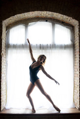 silhouette of a young good shaped ballerina standing on the huge window. Concept of healthy and...