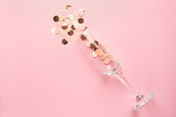 Champagne glass with pink and gold confetti on pink color paper background minimal style