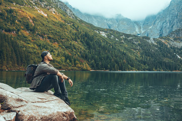 man sitting on the rock in front of lake in mountains enjoying the view - Powered by Adobe