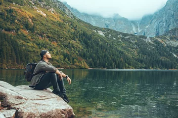 Foto op Plexiglas man sitting on the rock in front of lake in mountains enjoying the view © phpetrunina14
