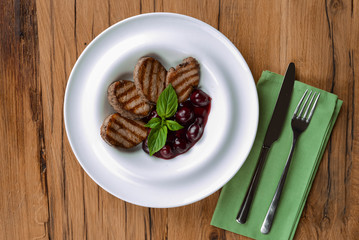 Grilled meat pieces with berry sauce served on a white plate over dark rustic wooden background. Italian cuisine.