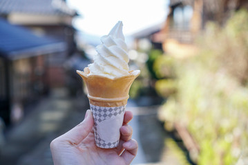 Naklejka premium Vanilla soft serve ice cream. Hand holding a cone of soft serve ice cream with vanilla flavor. outdoor