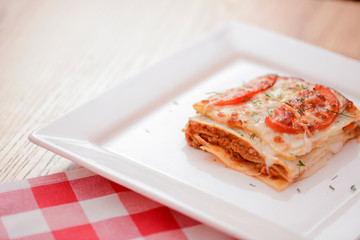 Small piece of tomato lasagna on a square white plate. Dinner in a restaurant, cafe or diner. Healthy food concept.