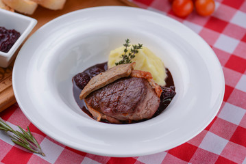 Mashed potato with meat and gravy served in a white plate over red plaid tablecloth.