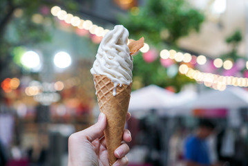 Woman holding a wafer cone of vanilla soft ice cream. soft ice cream melting. Blurred background.