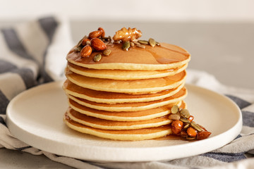 Stack of delicious pancakes with chocolate, honey, nuts and slices of banana on plate and napkin on wooden background