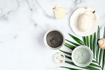 SPA natural organic cosmetic clay mask and powder in bowls and tropical palm leaf on marble table. Beauty products for face skin care and treatment concept.