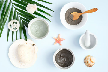 Fototapeta na wymiar SPA natural organic beauty products for face skin care and treatment. Cosmetic clay mask and powder in bowls, homemade soap and tropical palm leaf on pastel blue background. Top view, flat lay.