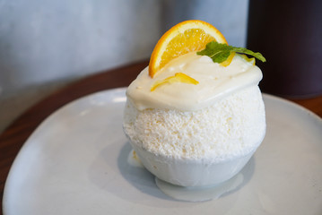 Yuzu Bingsu. A bowl of milk shaved ice topped with yuzu cream flavour and yuzu sliced on white plate at dessert cafe.