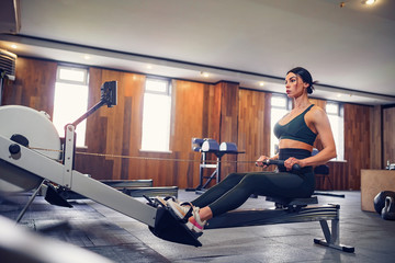 Determined young woman working out on row machine in fitness studio.
