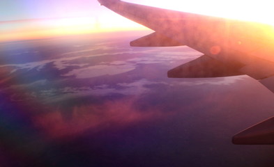evocative image of a wing of an airplane flying in backlight at sunset from the window with the earth in the background
