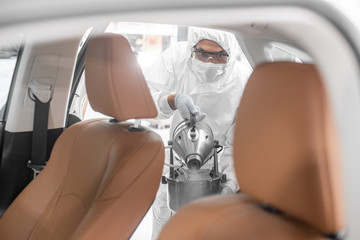Disinfectant worker character in protective mask and suit sprays bacterial or virus in a car.