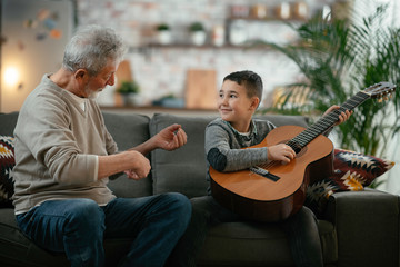 Obraz premium Grandpa and grandson playing guitar. Grandfather and grandson enjoying at home.