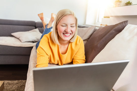 woman is relaxing on comfortable couch and using laptop at home.Portrait of beautiful young woman working on laptop while lying on sofa. Female using laptop at home.