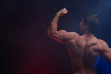 Muscular man showing muscles isolated on the black background with colored smoke. Concept of healthy lifestyle 