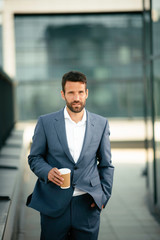 Young handsome man drinking coffee outdoors. Businessman in a blue suit.