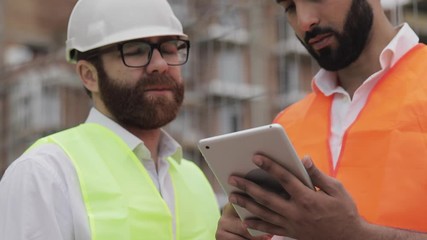 Close up of architect hands using tablet near construction site. The builder and architect man are discussing the construction plan of the modern business center.