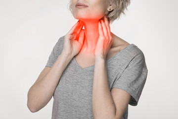 Female checking thyroid gland by herself. Close up of woman in white t- shirt touching neck with...