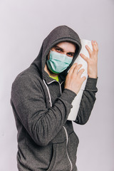 A guy in a gray sweatshirt and with rolls of toilet paper is standing on a white background. The excitement during quarantine for coronavirus. Rotaviruses in a man in a medical mask.