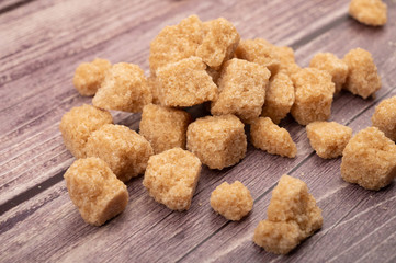Pieces of brown cane sugar scattered on a wooden background. Close up.