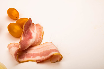 Sliced bacon and tomatoes on a white background. Close up.