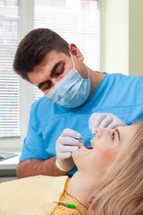 Dentist examining patient's teeth, wearing blue uniform and gloves, looking at patient's teeth carefully with dental instruments