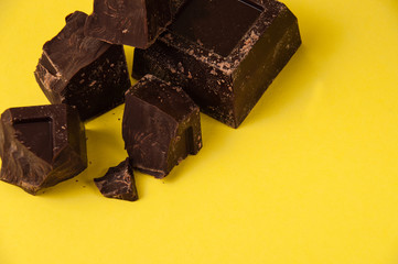 Appetizing pieces of black chocolate isolate on a yellow background close-up, copy space from right