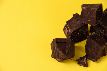 Appetizing pieces of black chocolate isolate on yellow background close-up, copy space with left