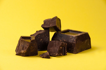 Pieces of black chocolate isolate on a yellow background close-up, copy space