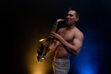 Fototapeta na wymiar Muscular man with naked torso playing on saxophone with smoked colorful background 