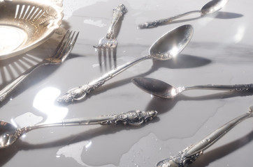 Closeup of shiny silver kit of spoons, forks, vintage plate on the wet white table.Concept of luxury event in the evening 