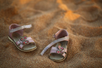 Lovely baby shoes with pink bows butterflies on sunlit sunset sandy beach, place for your text